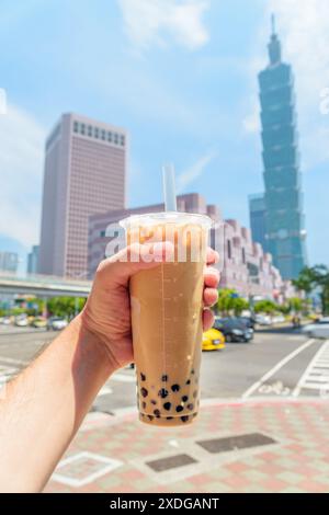 Blick auf die männliche Hand, die traditionellen taiwanesischen Bubble Milk Tee in der Innenstadt von Taipei, Taiwan, hält. Der Wolkenkratzer ist im Hintergrund sichtbar. Stockfoto