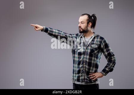 Bärtiger Mann, der beschuldigt zeigt, Hand auf Hüfte, mit einem ernsten Ausdruck, der Konflikte, Frustration und Wut zeigt, Durchsetzungskraft und Selbstvertrauen ausstrahlt Stockfoto