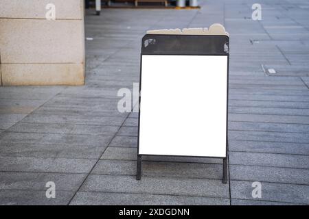 Leere, weiße Außenwerbeständer oder Sandwichplatte als Mustervorlage. Klare Straßenschilder neben einem Essbereich im Freien eines Restaurants Stockfoto