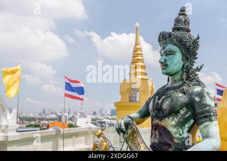 Buddhistische Statue im Tempel Wat Saket auf dem Goldenen Berg. Die Flagge des Königreichs Thailand, die über Bangkok flattert, ist im Hintergrund sichtbar. Stockfoto