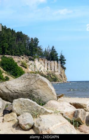 Blick auf die Klippe in Gdynia Orłowo an einem sonnigen Sommermorgen. Ruhige Ostsee. Große Felsbrocken im Vordergrund. Polen, Pommern, Gdynia. Stockfoto