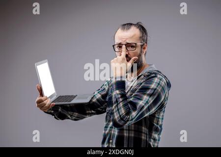 Ein besorgter Techniker behebt einen Laptop-Fehler in einem grauen Studio und hebt die Herausforderungen der Technologie und den Bedarf an Unterstützung bei der Computerrepai hervor Stockfoto