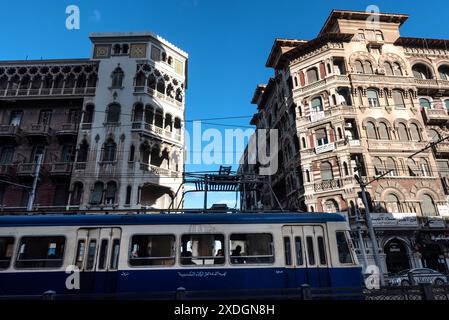 Historische Architektur und alte Straßenbahn, die in der typischen Alexandria Straße vorbeifährt. Alexandria, die zweitgrößte Stadt in der nördlichen Delta-Region Ägyptens, ist aufgrund des steigenden Meeresspiegels vom Untergang bedroht. Stockfoto