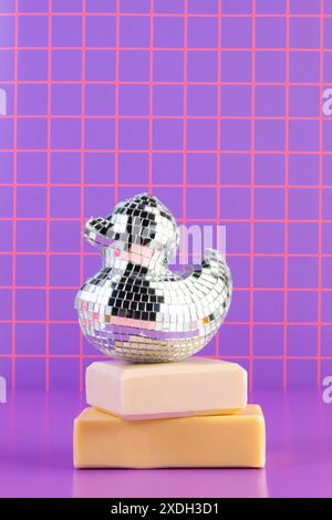 Disco Ball Gummiente auf gestapelten Seifenstäben, neonvioletter Hintergrund Stockfoto