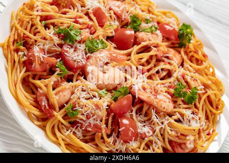 Garnelen fra diavolo mit Spaghetti, Tomatensoße, bestreut mit geriebenem Parmesankäse auf weißer Platte auf weißem Holztisch, Nahaufnahme, niederländisch Stockfoto