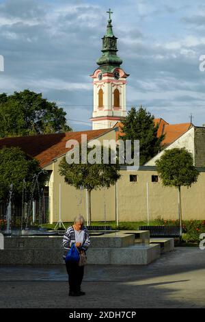 Alte Frau auf Hintergrund der Glockenturm der Kirche St. Georg in Sombor, Vojvodina, Serbien Stockfoto