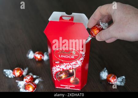 Die Hand des Mannes nimmt einen Lindor-Schokoladentrüffel aus einer roten Lindt-Schokoladenschachtel. Lindt ist ein Schweizer Chocolatier- und Süßwarenunternehmen, das 1845 gegründet wurde Stockfoto