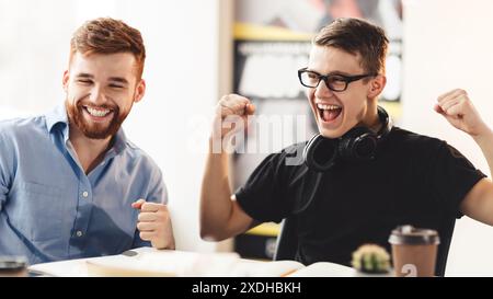 Zwei Männer feiern am Schreibtisch im Büro Stockfoto