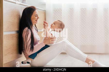 Frau Mutter, die das Baby hält, während sie auf dem Boden sitzt Stockfoto