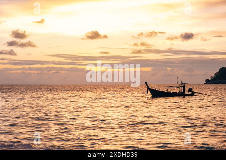 Silhouette eines traditionellen thailändischen Longtail-Bootes, das während eines atemberaubenden goldenen Sonnenuntergangs auf der Insel Phuket, Thailand, auf dem Meer schwimmt Stockfoto