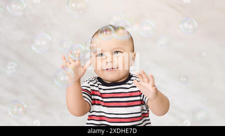 Das lächelnde Baby greift nach Seifenblasen im White Studio Stockfoto