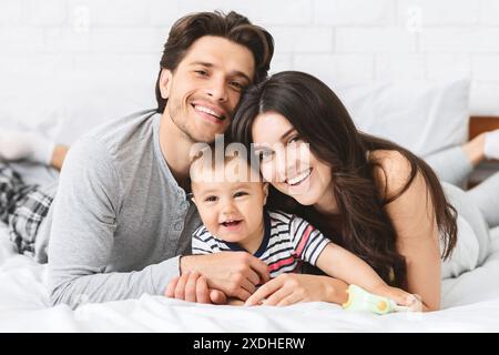 Glückliches Familienporträt der Eltern und des Babys, die auf dem Bett liegen Stockfoto