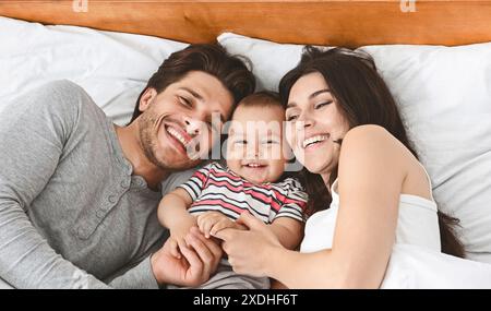 Glückliche Dreierfamilie, die gemeinsam im Bett lacht Stockfoto
