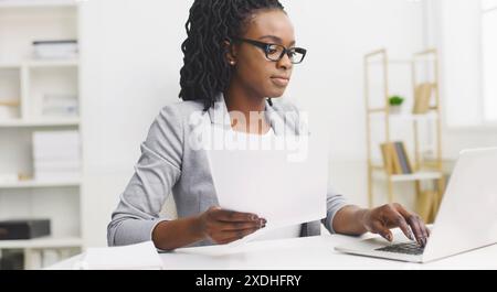 Fokussierte schwarze Frau, die Papierkram am Schreibtisch macht Stockfoto