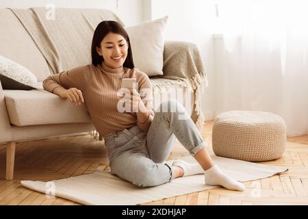Happy Asian Girl Messaging am Telefon zu Hause Stockfoto