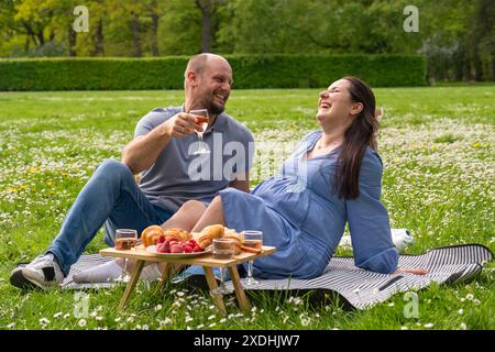 Glückliches schwangeres Paar, das Zeit zusammen auf einem Picknick im Freien verbringt. Sie lachen fröhlich. Sie sind glücklich. Die Familie erwartet ein Kind. Schwangerschaft. Fam Stockfoto