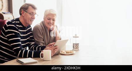Seniorenpaar, die online surfen, während sie Kaffee und Leckereien zu Hause genießen Stockfoto