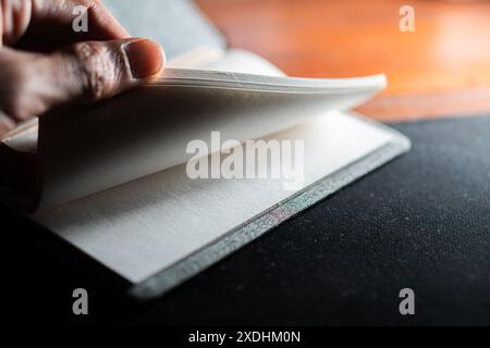 Nahaufnahme einer Person, die durch die Seiten eines Notizbuchs springt. Das Bild konzentriert sich auf die Hand und die Seiten mit einem unscharfen Hintergrund. Stockfoto