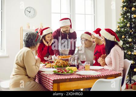Glückliche große Familie mit Kindern und Großeltern im Weihnachtsmann-Hut, der zu Hause am Weihnachtstisch sitzt. Stockfoto