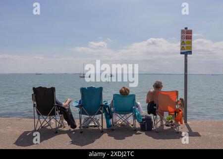 Southend on Sea, Großbritannien. Juni 2024. Vier Personen, die in zusammenklappbaren Campingstühlen sitzen, genießen einen sonnigen Tag am Meer mit Blick auf das ruhige Wasser mit Segelbooten. Ein auffälliges Sicherheitsschild am Strand warnt vor starken Strömungen, tiefem Wasser und rutschigen Oberflächen und verbietet Schwimmen und Tauchen. Heller Sonnenschein und Temperaturen um 23 °C bringen viele Menschen heraus, um das warme Wetter, die Küste und die Sonne in Southend zu genießen. Penelope Barritt/Alamy Live News Stockfoto