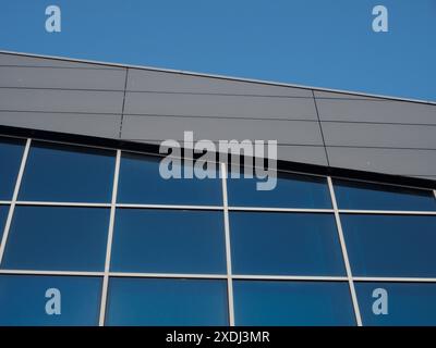 Hohes, modernes Bürogebäude mit blauen reflektierenden Fenstern, die an klaren Tagen im Sonnenlicht leuchten, mit elegantem, zeitgenössischem Design und urbanem Flair Stockfoto