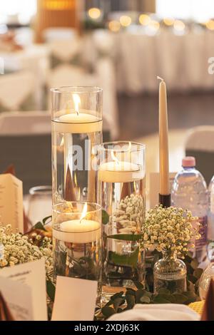 Kerzen mit sanfter Beleuchtung in Glasvasen mit Blumen schaffen ein romantisches Ambiente an einem Hochzeitsort Stockfoto