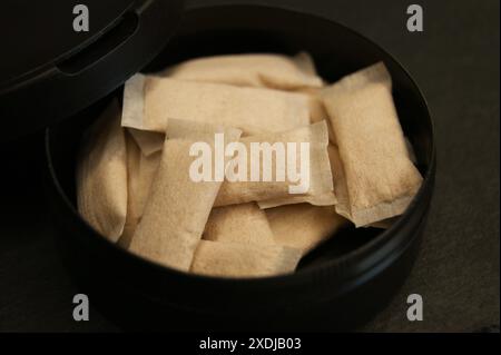 Eine offene Kiste mit Nikotinbeuteln. Nikotinbeutel in schwarzer Verpackung auf dunkler Oberfläche. Stockfoto