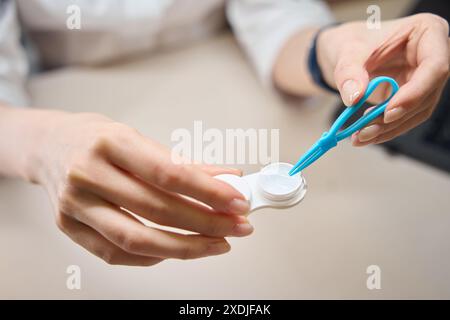 Frau nimmt eine transparente Linse aus dem Behälter mit Pinzette Stockfoto