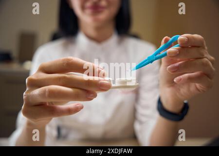 Optics-Mitarbeiter nimmt mit einer Pinzette eine Linse aus dem Behälter Stockfoto