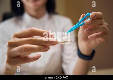 Lady nimmt eine transparente Linse mit Pinzette aus dem Behälter Stockfoto