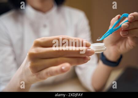 Der Berater nimmt die transparente Linse mit einer Pinzette aus dem Behälter Stockfoto