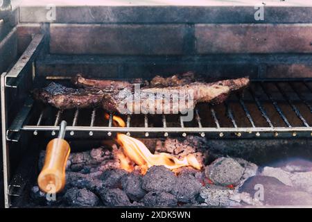 Eine Nahaufnahme eines Grills mit drei dicken Steakstücken, die über heißen Kohlen gekocht werden. Die Flammen sind unter dem Grillgitter sichtbar Stockfoto