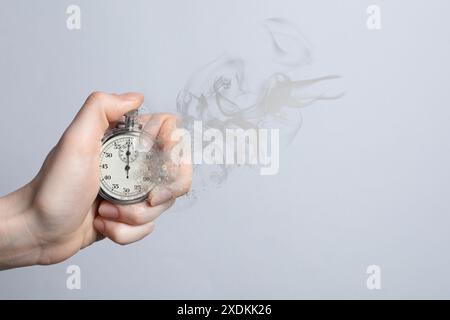 Frau mit auflösendem Chronometer auf grauem Hintergrund, Nahaufnahme. Die Zeit läuft ab Stockfoto