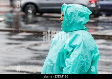 Ein Mann mit einem regenumhang steht auf einer Straße bei starkem Regen, Berlin, 22.06.2024, Berlin, Berlin, Berlin, Deutschland Stockfoto