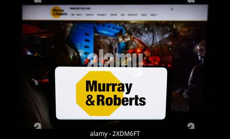 Person, die ein Mobiltelefon mit dem Logo des südafrikanischen Unternehmens Murray and Roberts Holdings Ltd. Vor der Webseite hält. Schwerpunkt auf dem Display des Telefons. Stockfoto