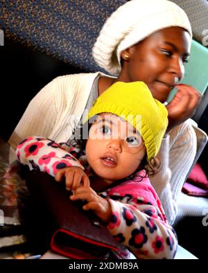 Die schwarze Mutter hat ihre wunderschöne Tochter mit braunen Augen auf ihrem Schoß Stockfoto