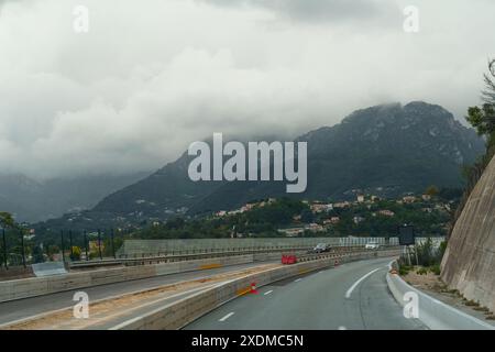 Ein Blick aus einem Auto, das auf einer Straße durch die italienischen Alpen fährt. Die Berge sind von Wolken bedeckt, und die Straße windet sich. Stockfoto