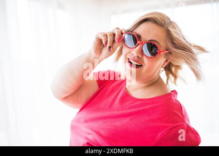 Porträt einer schönen jungen übergewichtigen Frau zu Hause, mit Sonnenbrille. Stockfoto