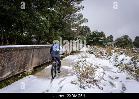 Radfahrer im Schnee neben dem Wasserkanal, dem Gorg Blau Reservoir, Escorca, Mallorca, Balearen, Spanien. Stockfoto