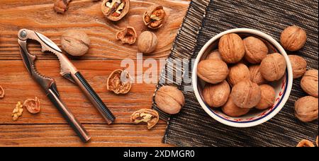 Schüssel mit Walnüssen und Nussknacker auf hölzernem Hintergrund, Draufsicht Stockfoto