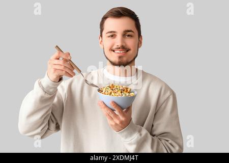 Schöner junger Mann, der leckere Müsliringe auf grauem Hintergrund isst Stockfoto