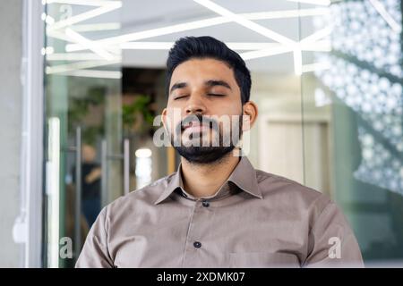 Ein ruhiger Mann mit geschlossenen Augen meditiert in einer modernen Büroumgebung. Dieser ruhige Moment fängt die Essenz von Stressabbau und Achtsamkeitsübungen in einem Arbeitsumfeld ein Stockfoto