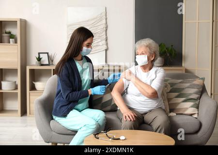 Junge Krankenschwester geimpft Seniorinnen zu Hause Stockfoto