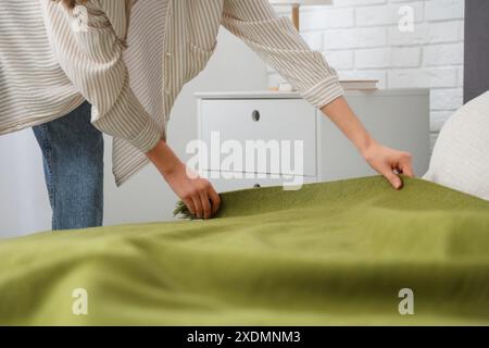 Junge Frau, die zu Hause grüne Decke auf das Bett legt, Nahaufnahme Stockfoto