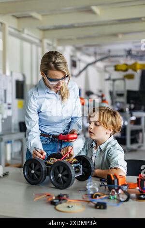 Eine Lehrerin hilft jungen Schülern beim Bau eines Roboterautos im Robotikclub. Kinder, die Robotik in der Grundschule lernen. Wissenschaft Stockfoto