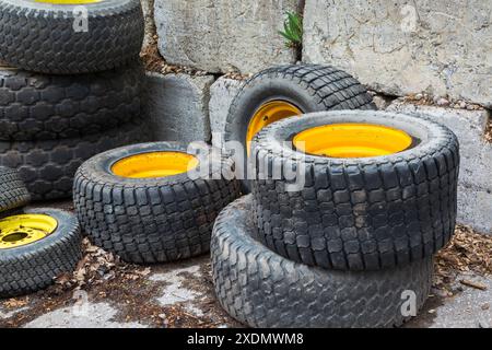 Verschiedene Kfz-Gummireifen mit gelben Felgen im Betonblock-Behälter auf dem Recyclingplatz im Freien. Stockfoto