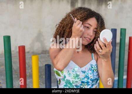 Junge Frau mit lockigem Haar, die sich mit einem Handspiegel schminkt Stockfoto