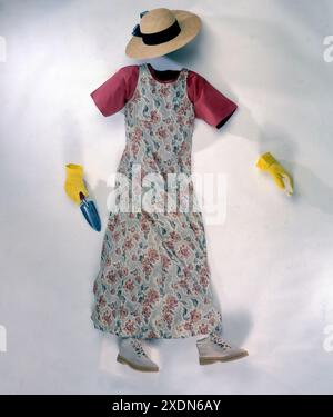 Flaches Blumenkleid, Strohhut, Handschuhe und kleine Gartengeräte auf weißem Hintergrund symbolisieren den Frühling, die Gartenarbeit und die lässige Arbeit im Freien Stockfoto