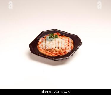 Penne Pasta in reichhaltiger Tomatensauce garniert mit Petersilie, serviert in einer dunklen achteckigen Schüssel auf weißem Hintergrund, einfache Studio-Präsentation. Stockfoto