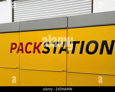 Kehl, Deutschland - April 2024: Nahaufnahme eines gelben Schildes mit dem Wort Packstation in schwarz-roten Buchstaben. Das Schild ist an einem Gebäude mit einem grauen Dach und einer weißen Wand im Hintergrund angebracht. Stockfoto